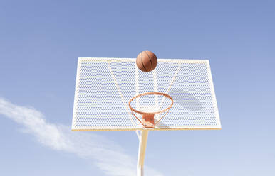 Ball over basketball hoop during sunny day - JCCMF01729