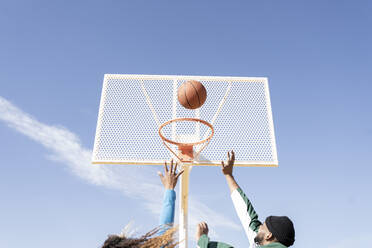 Male and female friends playing basketball on sunny day - JCCMF01730