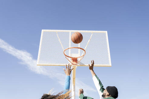 Männliche und weibliche Freunde spielen Basketball an einem sonnigen Tag - JCCMF01730