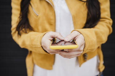 Mittlere erwachsene Frau in gelber Jacke, die eine Textnachricht über ihr Smartphone sendet - EBBF03085