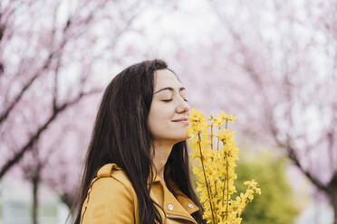 Smiling woman with eyes closed smelling fragrance of yellow flowers - EBBF03090