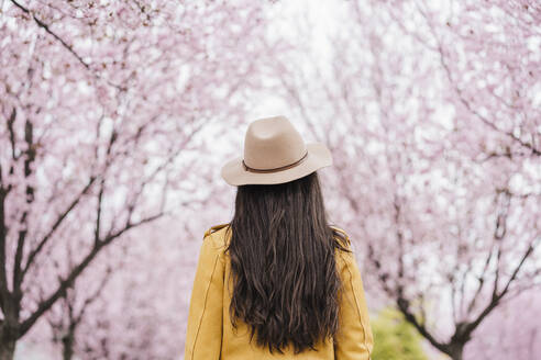 Frau mit Sonnenhut vor einem Mandelbaum im Frühling - EBBF03091