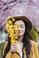 Lächelnde Frau mit geschlossenen Augen, die im Frühling gelbe Blumen hält - EBBF03095