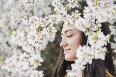 Lächelnde schöne Frau mit geschlossenen Augen durch Blumen im Frühling gesehen - EBBF03101