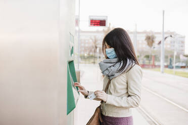 Frau mit Gesichtsschutzmaske beim Ticketkauf am Kiosk während der COVID-19 - EBBF03106
