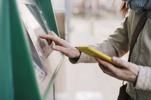 Woman operating kiosk while holding mobile phone - EBBF03109