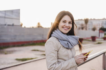 Lächelnde Frau mit Mobiltelefon am Bahnhof - EBBF03116