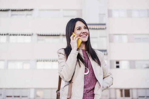 Lächelnde schöne Frau, die wegschaut, während sie mit einem Mobiltelefon spricht - EBBF03125