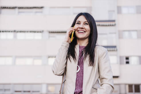Lächelnde Frau mit langen Haaren, die wegschaut, während sie mit einem Mobiltelefon spricht - EBBF03127