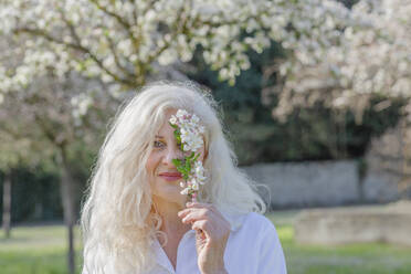Woman holding white flower while standing at park - EIF00752