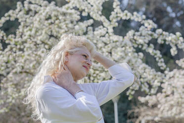 Reife Frau mit Händen in den Haaren schaut in den Park - EIF00753