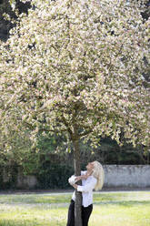 Fröhliche Frau mit umarmendem Baum im Park während des Frühlings - EIF00756