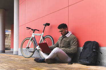 Männlicher Unternehmer, der einen Laptop benutzt, während er mit dem Fahrrad auf dem Gehweg sitzt - JAQF00447