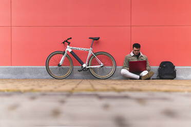 Businessman using laptop while sitting by bicycle on footpath - JAQF00448