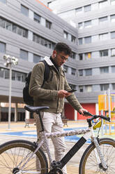 Junger Mann benutzt sein Smartphone, während er mit dem Fahrrad steht - JAQF00451