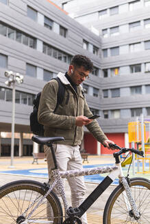 Junger Mann benutzt sein Smartphone, während er mit dem Fahrrad steht - JAQF00451