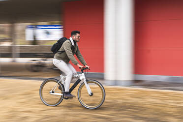 Handsome man riding bicycle by red wall - JAQF00452