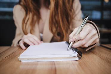 Frau schreibt in Tagebuch am Tisch in einem Café - EBBF03143