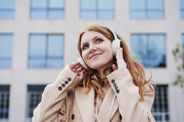 Beautiful redhead woman contemplating while listening music through headphones - EBBF03167