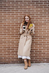 Lächelnde Frau mit Einweg-Kaffeebecher und Mobiltelefon auf dem Fußweg stehend - EBBF03172