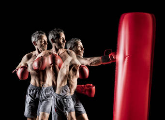 Älterer männlicher Boxer, der einen roten Sandsack vor einem schwarzen Hintergrund schlägt - STSF02902