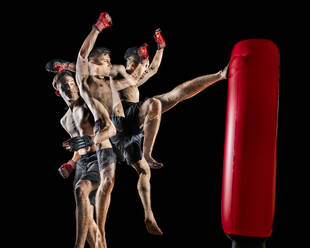 Junger hemdloser männlicher Kampfsportler, der einen Boxsack auf schwarzem Hintergrund tritt - STSF02904