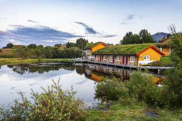 Norwegen, Vega-Archipel, Überwuchertes Haus mit Spiegelung im kleinen Teich - RUNF04263