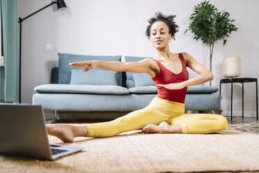 Frau macht Yoga, während sie zu Hause auf dem Laptop ein Online-Tutorial ansieht - JCZF00623