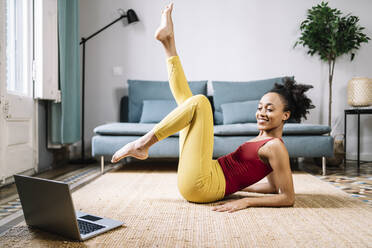 Smiling young woman exercising while watching tutorial on laptop at home - JCZF00624