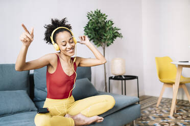 Happy woman listening music while sitting on sofa at home - JCZF00629