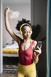 Cheerful woman listening music through smart phone at home - JCZF00632