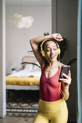 Junge Frau hört Musik, während sie sich zu Hause an die Wand lehnt - JCZF00633