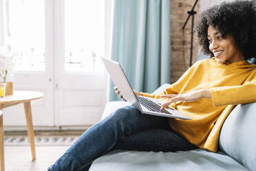 Young woman using laptop while sitting on sofa at home - JCZF00641