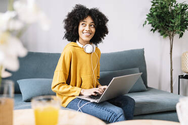 Nachdenkliche junge Frau mit Laptop, die zu Hause auf dem Sofa sitzt - JCZF00645