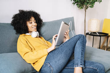 Relaxed young woman using digital tablet while sitting on sofa at home - JCZF00647