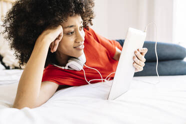 Young woman looking at digital tablet while lying on bed at home - JCZF00650