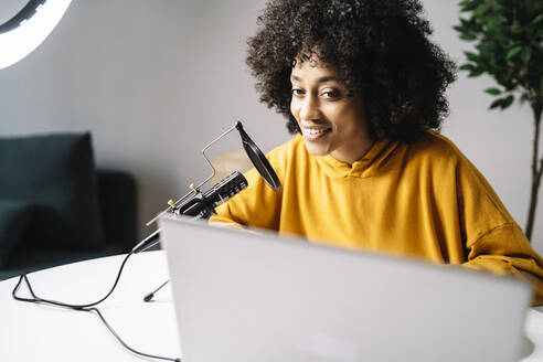 Young woman podcasting while looking at laptop at home - JCZF00669