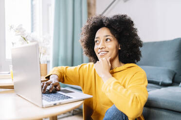 Thoughtful woman looking away while sitting by laptop at home - JCZF00676