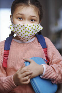 Girl in sweater wearing protective face mask holding pencil case during COVID-19 - AZF00226