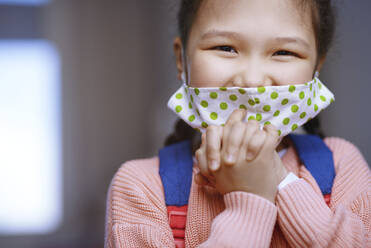 Girl with hands clasped wearing protective face mask during pandemic - AZF00227