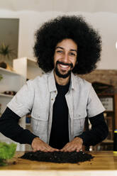 Smiling Afro man making kokedama plant on table at home - AFVF08478