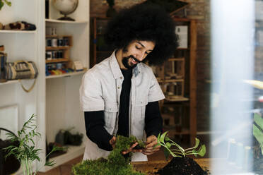 Man holding moss while preparing kokedama plant on table - AFVF08482