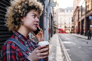 Curly haired woman having coffee while talking on smart phone - ASGF00163
