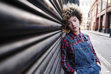 Hipster woman with hands in pockets leaning on shutter - ASGF00171