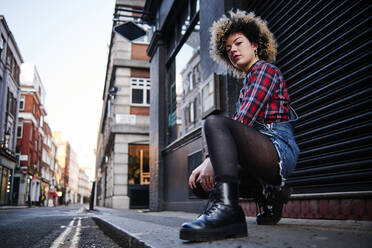 Young woman crouching on footpath in city - ASGF00177