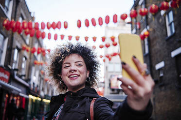 Lächelnde Hipster-Frau, die ein Selfie mit ihrem Smartphone in Chinatown macht - ASGF00183