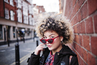 Curly haired woman wearing sunglasses by wall at Chinatown during vacations - ASGF00187