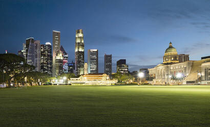 Singapur, Padang-Feld in der Abenddämmerung mit beleuchteter Stadtsilhouette im Hintergrund - AHF00349