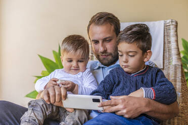 Father sharing smart phone with sons at home - DLTSF01716