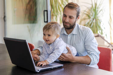 Smiling cute boy using laptop in front of father at table - DLTSF01721